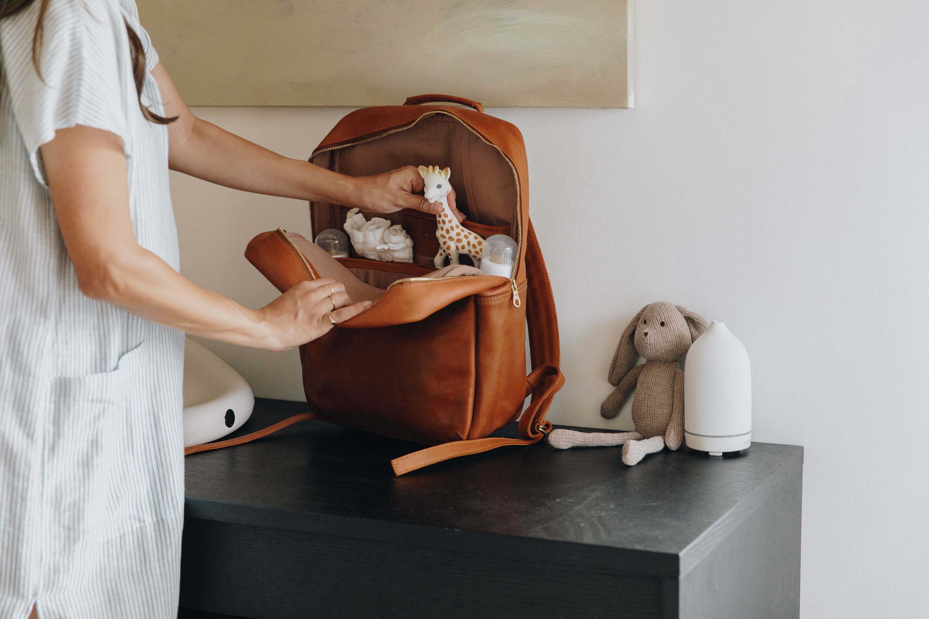 mom packing a brown leather diaper backpack with baby's items